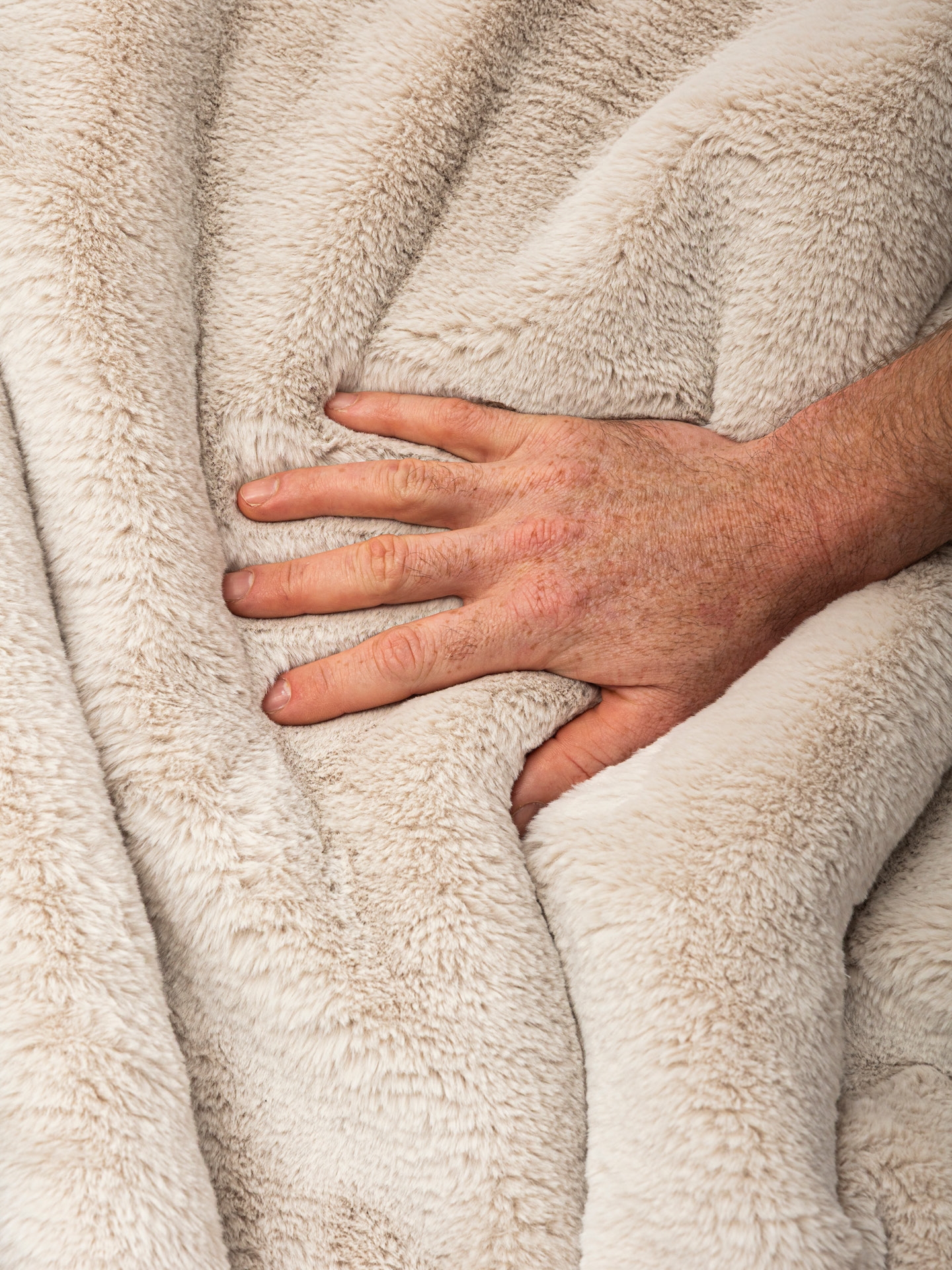 Hand pressing into pale faux fur blanket to show softness