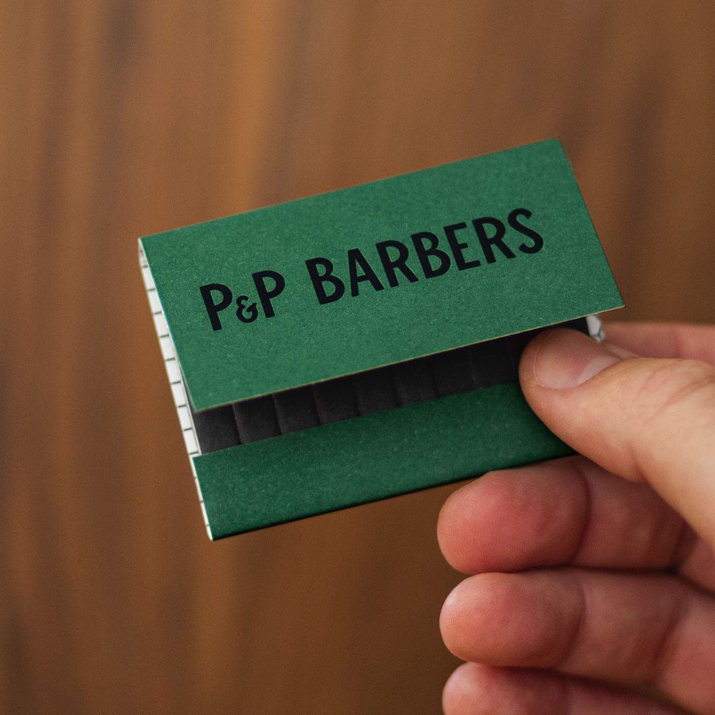 Front of green P&P Barbers branded matchbox held in hand