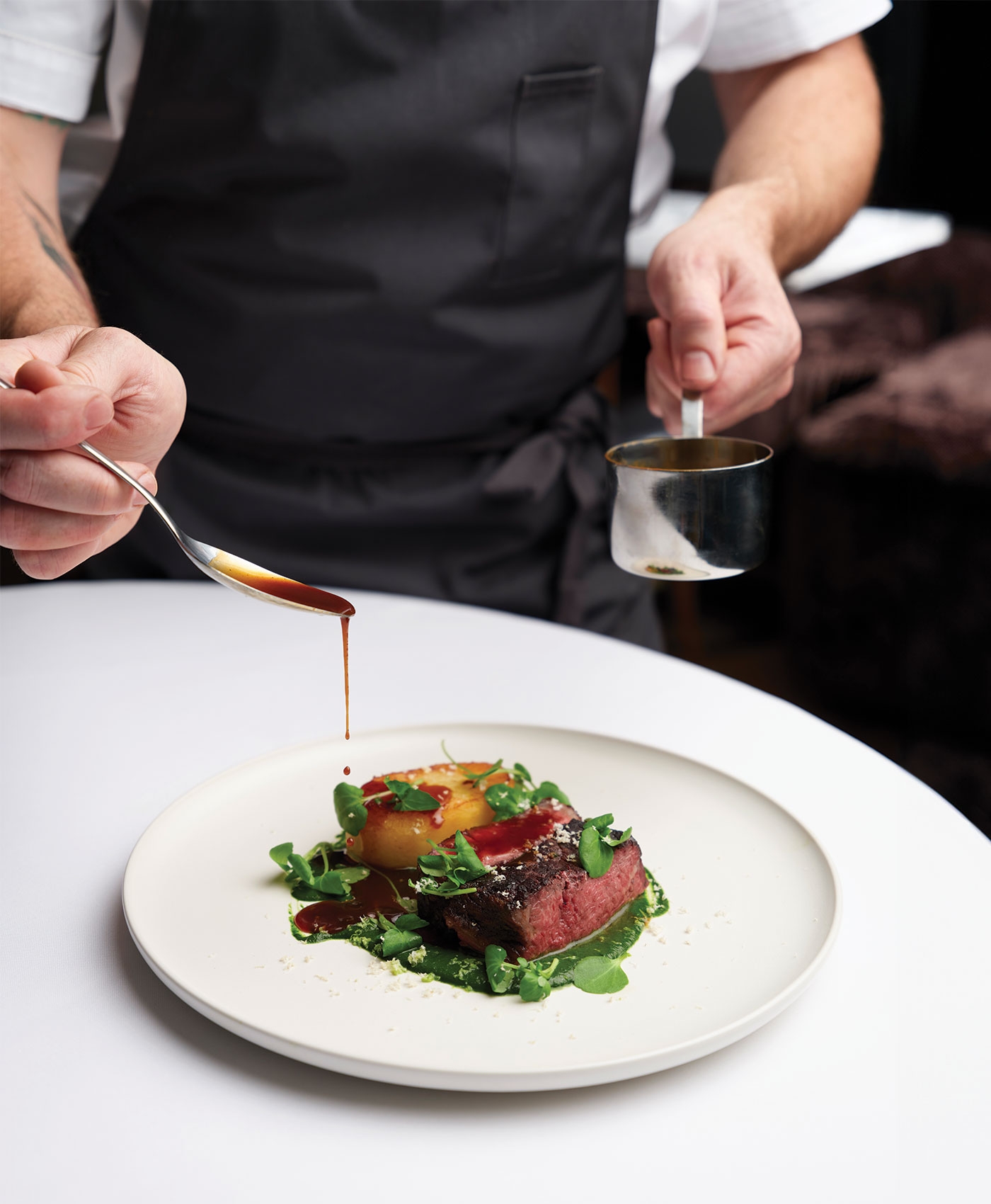 Chef spooning Bone Roasters jus over a plated beef dish