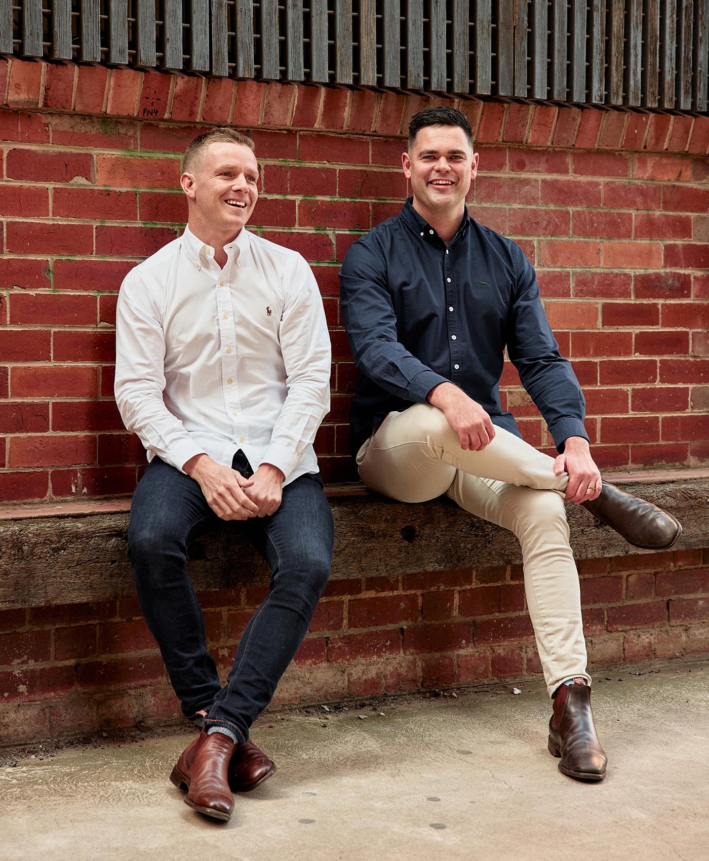 Andrew Chalkley and Jeremy Musso seated against a red brick wall